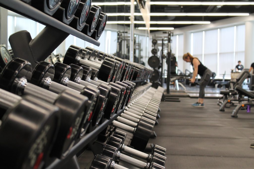 complete set of dumbbell weights in a gym with woman working out in the background