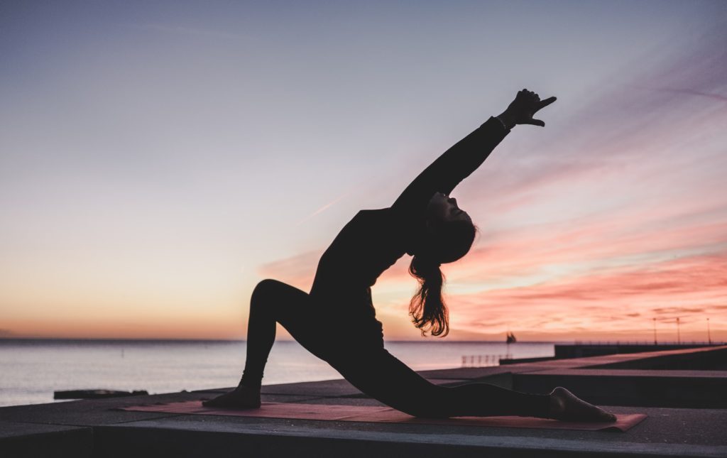 silhouette of a woman doing yoga outdoors in the evening after sunset by the harbor