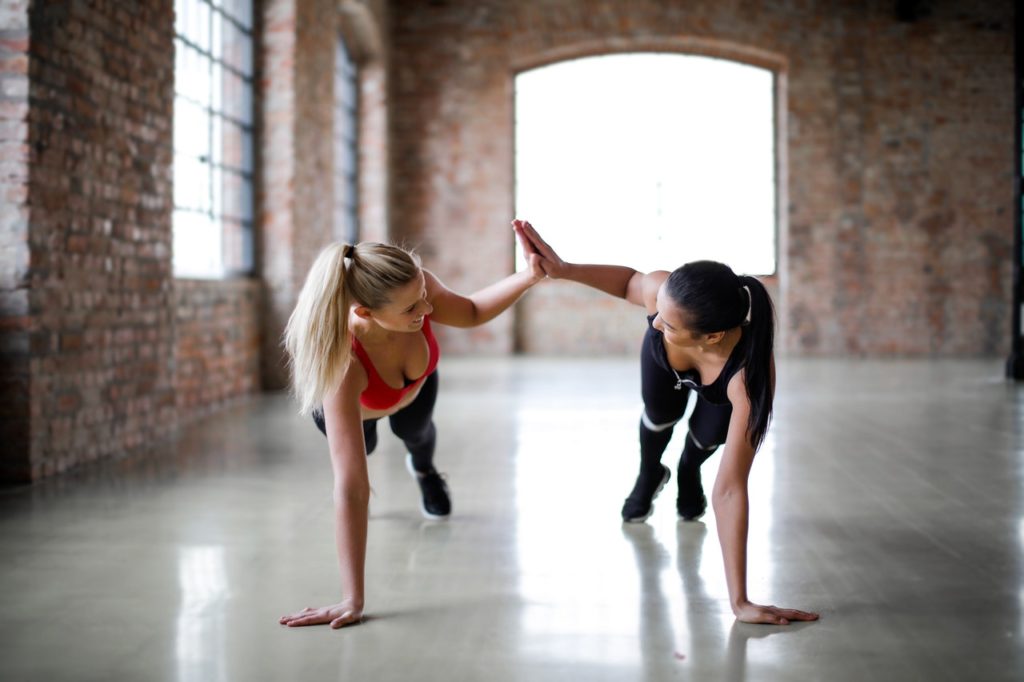 two fit women high fiving while doing floor exercises, gym buddies planking