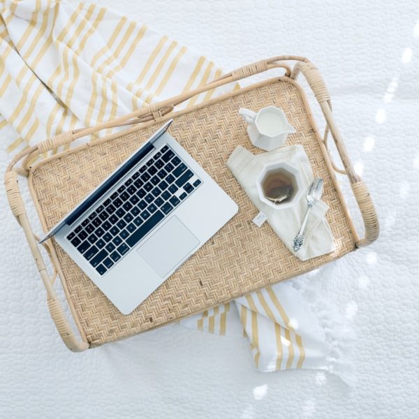 top view of laptop and cup of tea on a rattan tray on top of a blanket