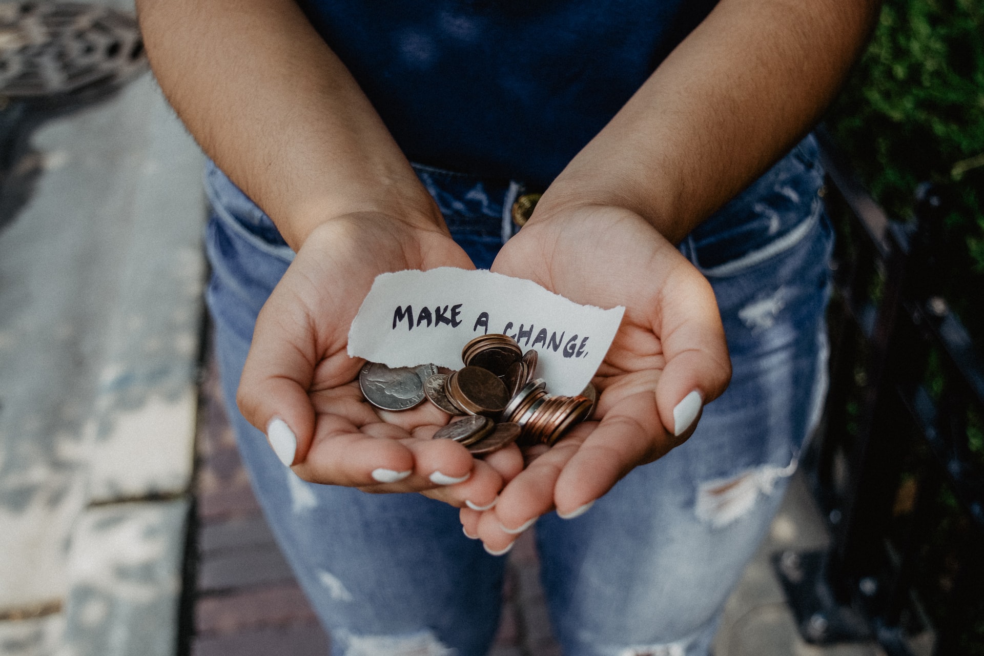 Person holding a handful of coins and a piece of paper that says "make a change"