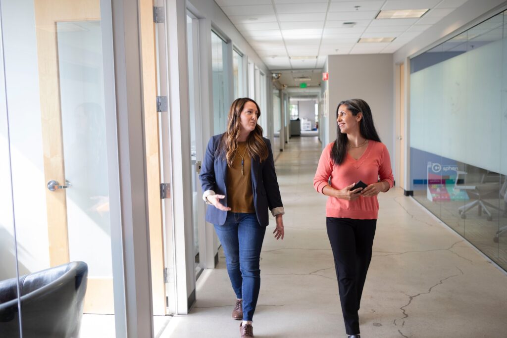 Two professional women walking down a hall and talking