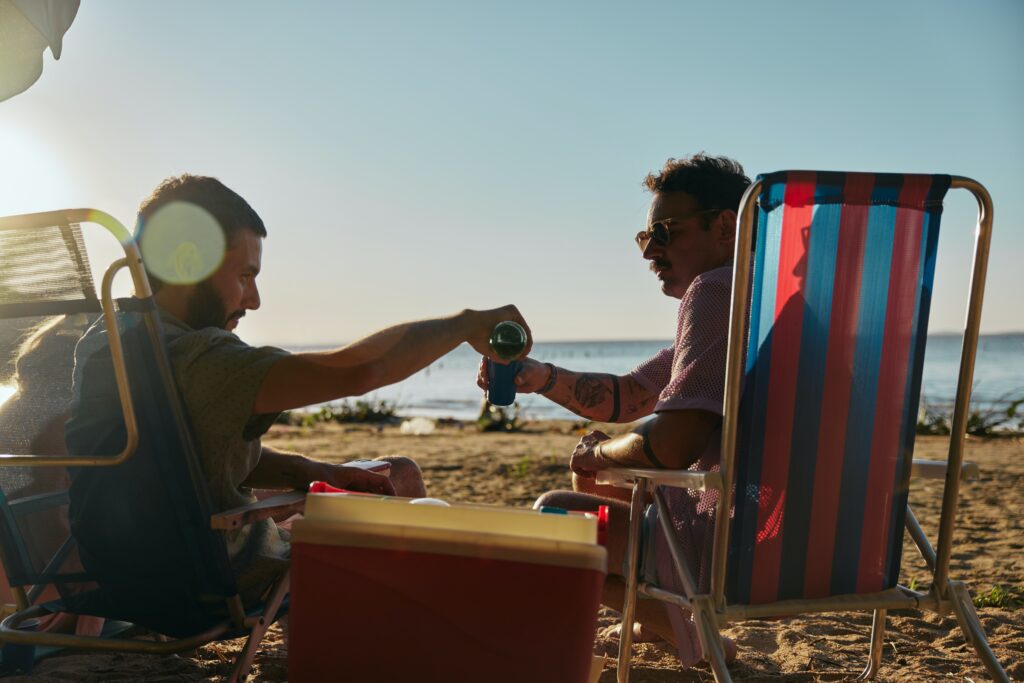 Two men relaxing on a beach, pouring a drink