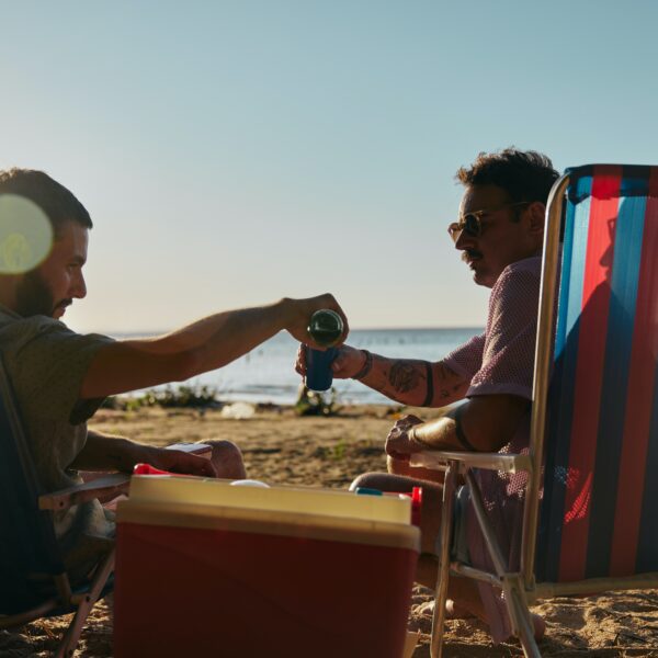 Two men relaxing on a beach, pouring a drink